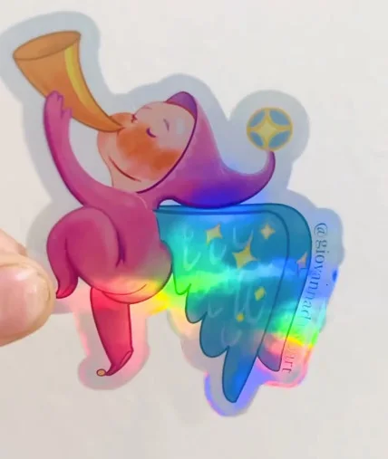 Photo of a holographic sticker of a pink figure in a pointed hat blowing a long horn, with a rainbow starry cape.