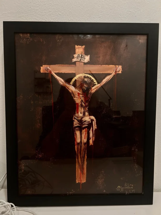 Framed painting of Christ crucified with a gold halo beneath an IC XC NIKA plaque, against a dark background.