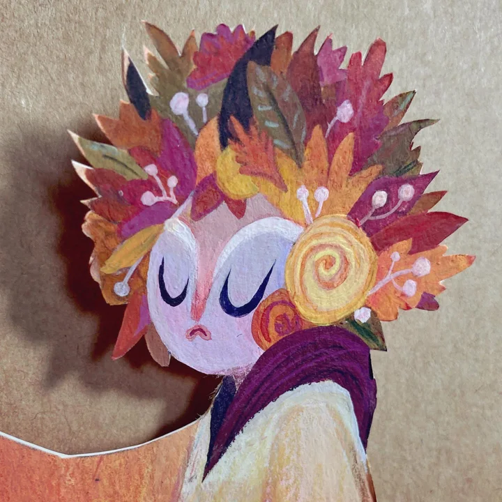 Layered paper-cut sprite with closed eyes beneath a towering crown of red, orange, and purple autumn leaves.