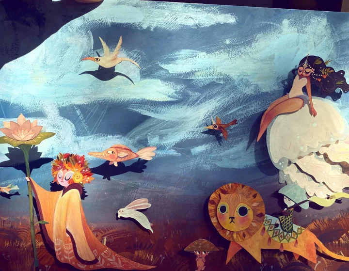 Layered paper cut-outs of a robed girl, a lion, birds, and a mermaid on a jellyfish against a blue painted sky.