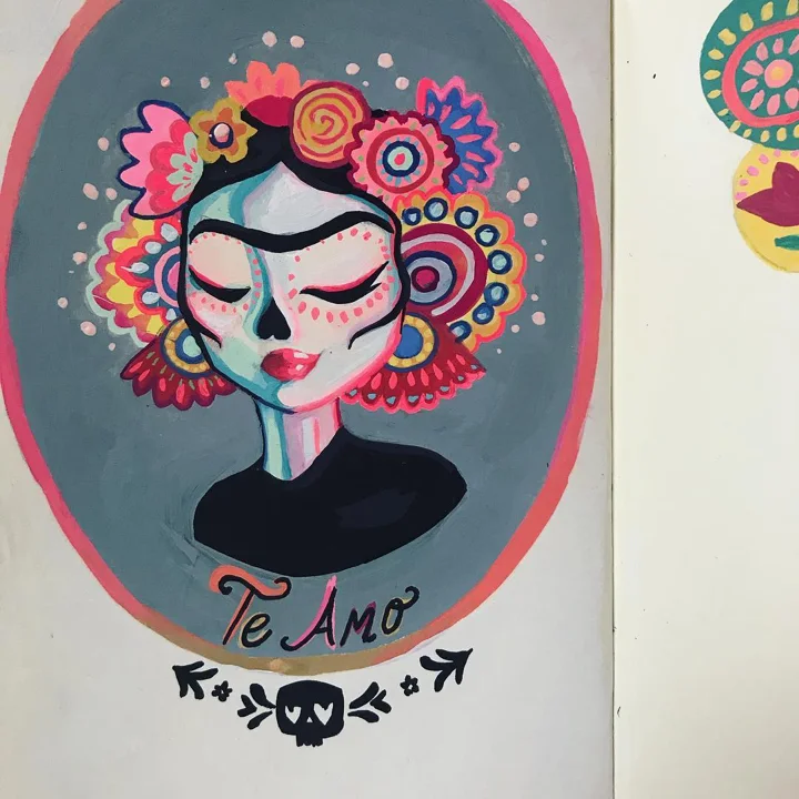 Painting in a sketchbook of a woman with sugar-skull face paint and a bright flower crown above the words Te Amo.
