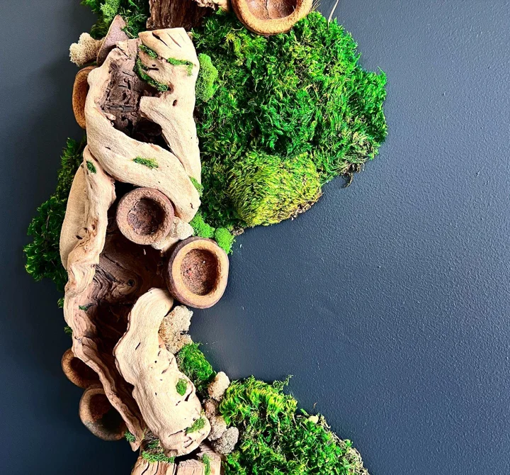 Photo of a wall-mounted wreath of twisted driftwood and clustered moss against a navy blue wall.