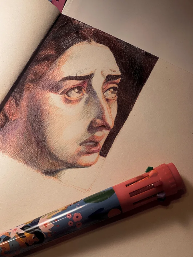 Ballpoint drawing of a dark-haired woman's anguished face looking up and aside, on a sketchbook page beside a pen.
