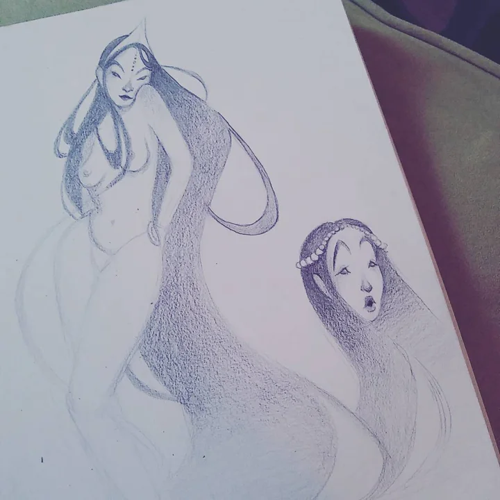 Pencil sketch of two long-haired mermaids, one wearing a pearl headband, on a tilted sketchbook page.